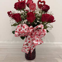 Red roses in a dark vase with a heart-patterned bow and Valentine topper