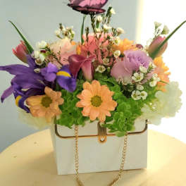 Colorful flower arrangement in a white handbag-shaped container