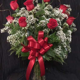 Red roses and baby's breath in a glass vase with a red bow