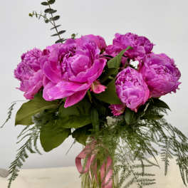 Pink peonies arranged in a clear glass vase with trailing greenery
