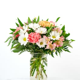 Mixed bouquet of white daisies, pink carnations, and peach blooms in a clear glass jar vase