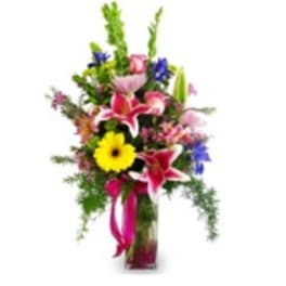 Tall mixed flower arrangement in a glass vase with bright pink and yellow blooms