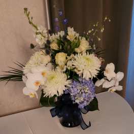 White and lavender floral arrangement in a dark vase with a ribbon