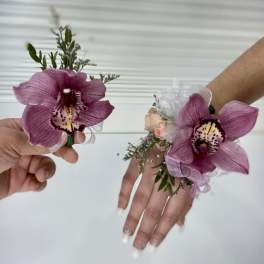 Two purple orchid wrist corsages held in hands.