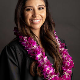 Woman wearing a purple orchid lei over a black graduation gown