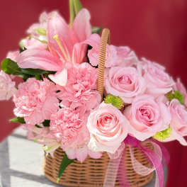Pink roses and carnations in a wicker basket with ribbon
