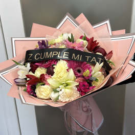 Mixed bouquet of pink, red, white, and yellow flowers wrapped in pink paper