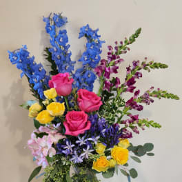 Colorful mixed bouquet in a clear glass vase with tall blue and purple blooms