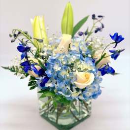 Blue hydrangeas and cream roses in a glass vase with tall lilies
