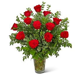 Red roses arranged in a clear glass vase with mixed greenery