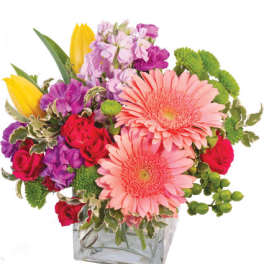 Mixed bouquet with pink gerberas, roses, tulips, and purple blooms in a glass vase