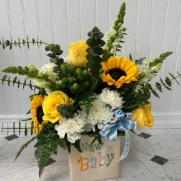 Yellow roses and sunflowers in a baby-themed container with a blue ribbon.