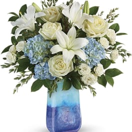 White lilies, roses, and blue hydrangeas in a blue glass vase