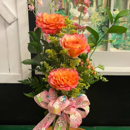Tall bouquet of orange roses in a clear glass vase with a pink ribbon