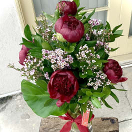 Bouquet of deep red peonies with pink filler flowers in a glass vase