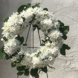 White floral wreath on a stand with dark green leaves
