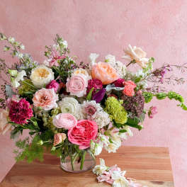 Mixed bouquet of pink, peach, white, and green flowers in a clear glass vase