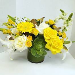 Yellow and white floral arrangement in a green glass vase