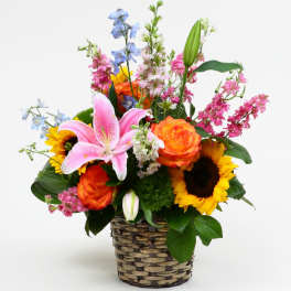 Mixed bouquet in a woven basket with lilies, roses, and sunflowers