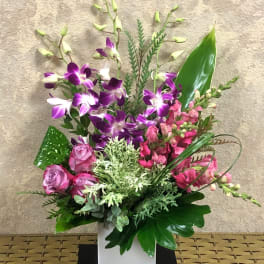 Purple orchids and pink flowers arranged in a white square vase