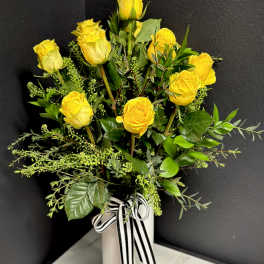 Yellow roses arranged in a white vase with a black-and-white ribbon
