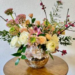 Mixed bouquet of roses, hydrangea, and orchids in a gold bowl vase