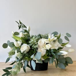 White floral arrangement in a black vase with eucalyptus and succulents