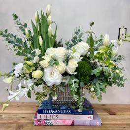 White roses and lilies arranged in a silver vase with green foliage