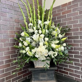 Tall white arrangement with lilies and roses in a basket on a pedestal