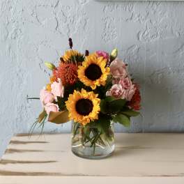 Bouquet of sunflowers and pink flowers in a clear glass vase