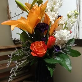 Orange lilies and white flowers in a tall vase