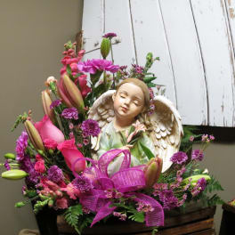 Pink and purple floral arrangement with an angel figurine and ribbon
