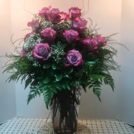 Pink roses arranged in a tall glass vase with greenery