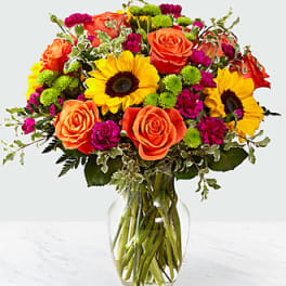 Bright mixed bouquet with roses and sunflowers in a clear glass vase