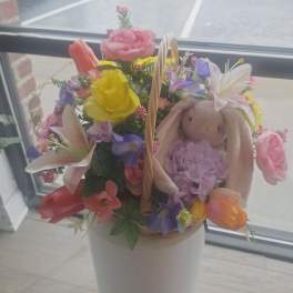 Basket of mixed pink, yellow, and purple flowers with a plush bunny tucked among the blooms