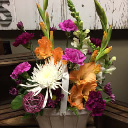 Colorful mixed flower arrangement in a white basket with a ribbon