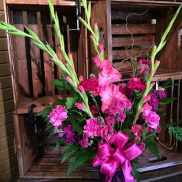 Pink floral arrangement with tall gladiolus in a dark vase and ribbon