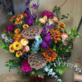 Tall mixed bouquet with purple, orange, and yellow flowers in a red vase