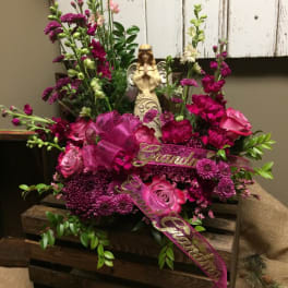 Pink and magenta floral arrangement with a figurine and ribbon in a wooden crate