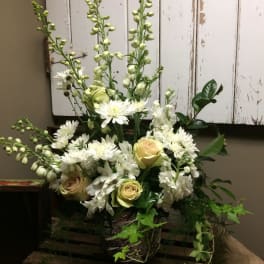 White floral arrangement with roses and tall spires in a rustic basket