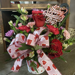 Valentine bouquet with red roses, pink carnations, and purple daisies in a heart-print tin