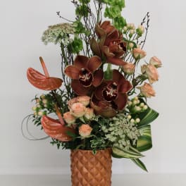 Tall arrangement with brown orchids, peach roses and tropical blooms in a textured terracotta vase