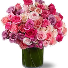 Arrangement of pink, white, and lavender roses in a clear cylinder vase wrapped with green leaves