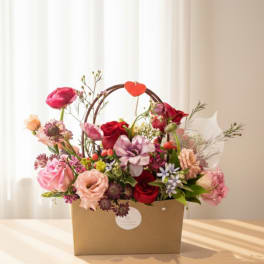 Mixed pink and red flower arrangement in a brown gift box with a heart handle