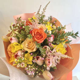 Bouquet of orange, peach, pink, and yellow flowers wrapped in coral paper
