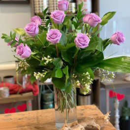 Lavender roses arranged in a clear glass vase with greenery