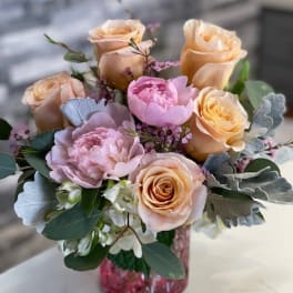 Peach and pink roses arranged in a pink glass vase