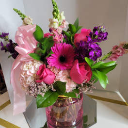 Pink and purple mixed bouquet in a pink glass vase with a ribbon
