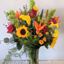 Mixed bouquet with sunflowers, roses, and calla lilies in a glass vase