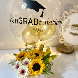 Graduation balloon above a sunflower and daisy arrangement